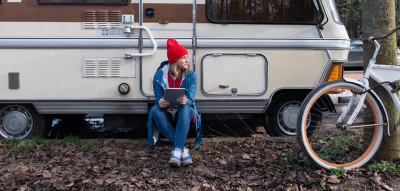 Lady sitting in front of RV in a campground and working on her tablet