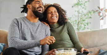 Una pareja sonriendo sentada en un sofá de la sala de estar con un bol de palomitas de maíz