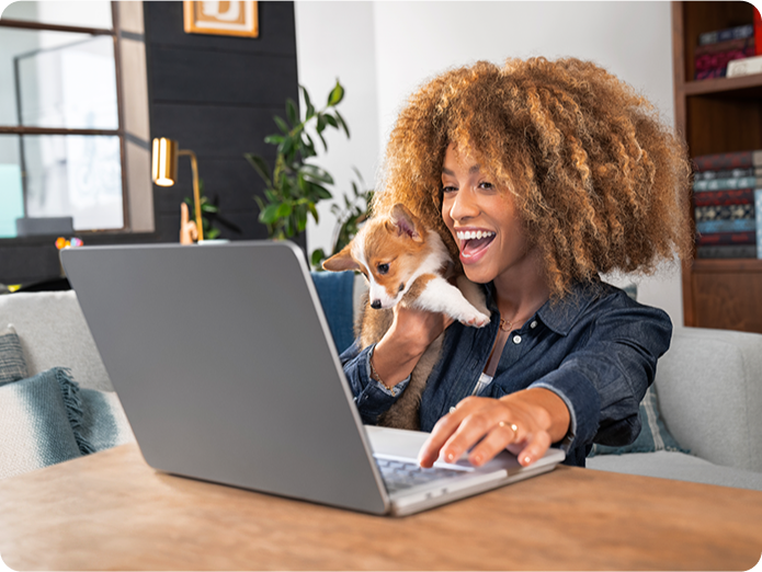 Mujer sonriendo frente a una laptop y con un perro en brazos