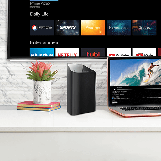 Módem Panoramic WiFi de Cox sobre una mesa con una tablet abierta y una TV en la pared mostrando el contenido de Contour TV