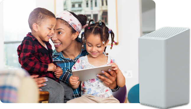 Una mujer con una niña y un niño, sentados en la sala miran una tablet sonrientes