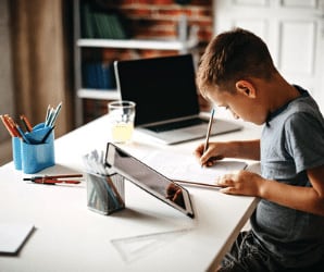 Boy at desk writing, using laptop and tablet