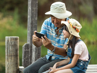 An elderly man holding a phone and showing it to a small kid