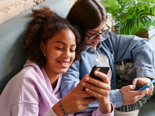 Two girls sitting together looking at their phones