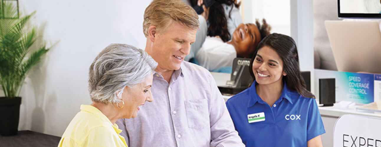 Elderly couple smiling with Cox employee looking at mobile devices