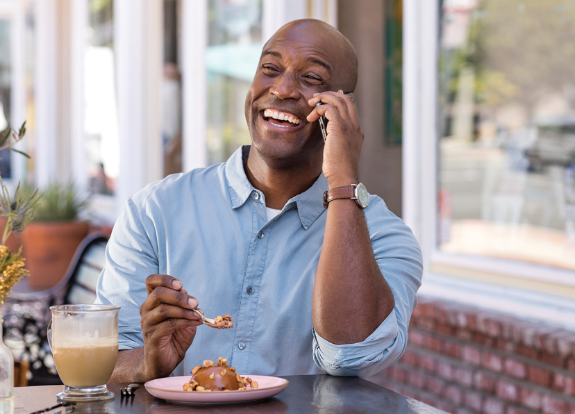 Man laughing eating outside talking on mobile device