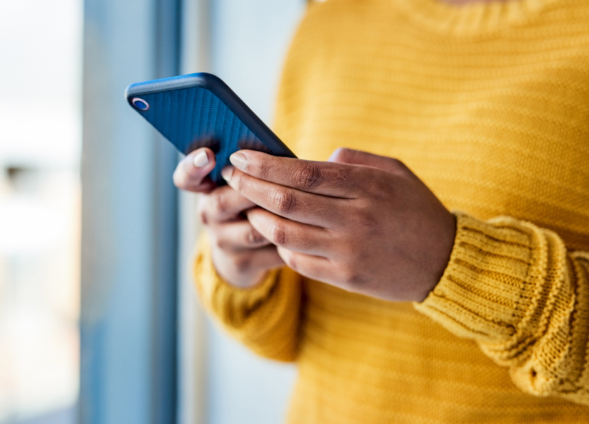 Woman in yellow sweater holding mobile device in hands