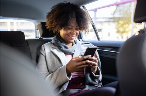 Woman sitting in car smiling texting on mobile device