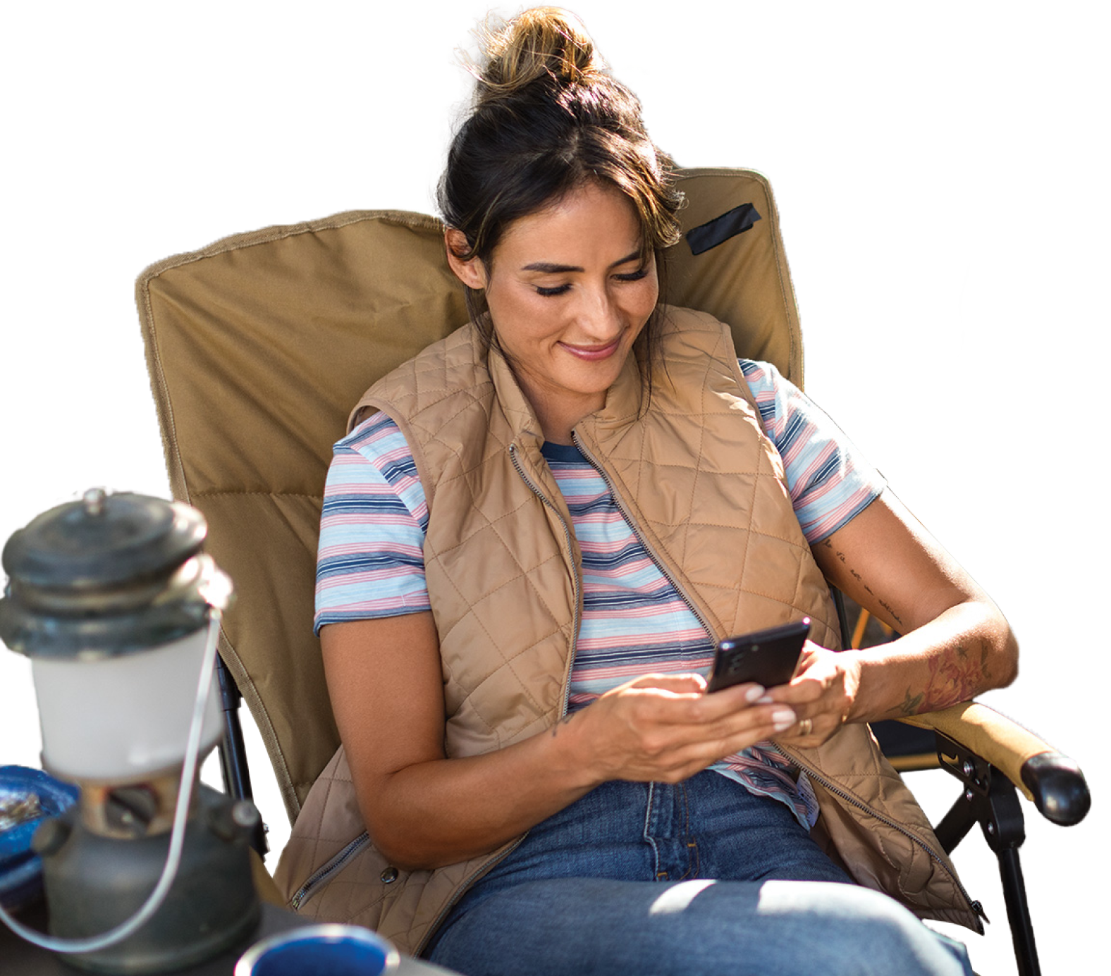 Mujer sentada en una silla de camping junto a una mesa en un entorno al aire libre mirando un equipo móvil.