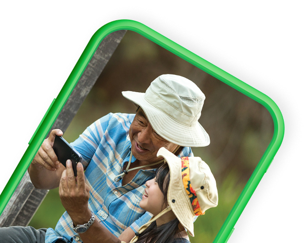 Mobile phone top half silhouette in green slanted right with father and daughter sitting on dock looking at mobile device on screen