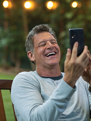 man-on-bench-laughing-while-looking-at-cellphone